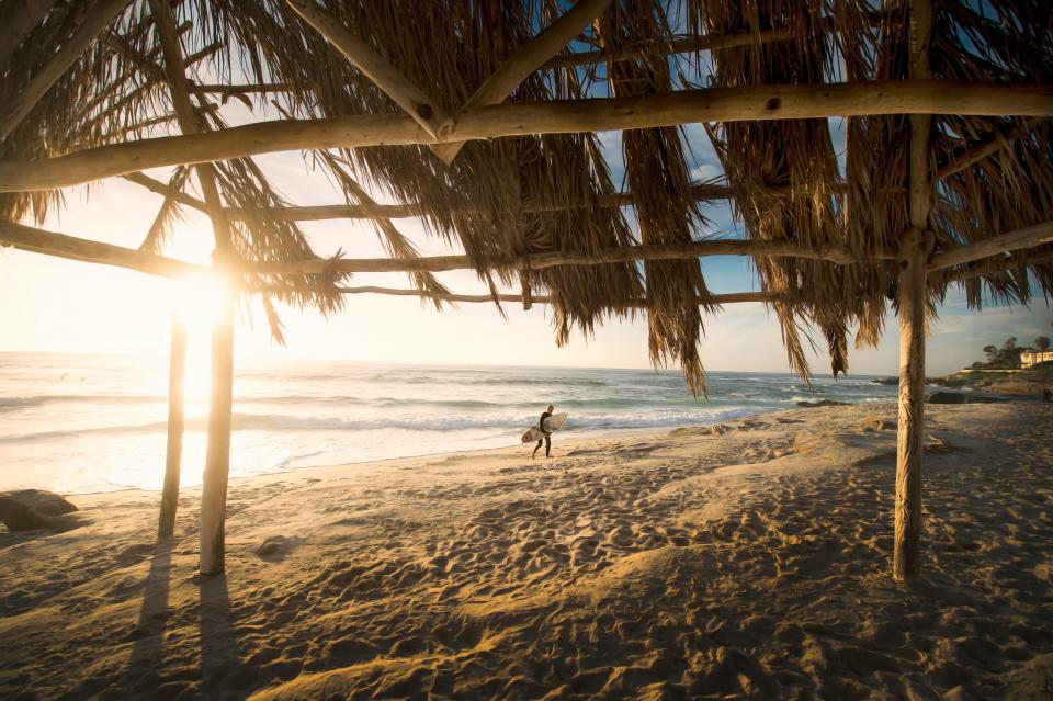A surfer walking toward the ocean at sunset